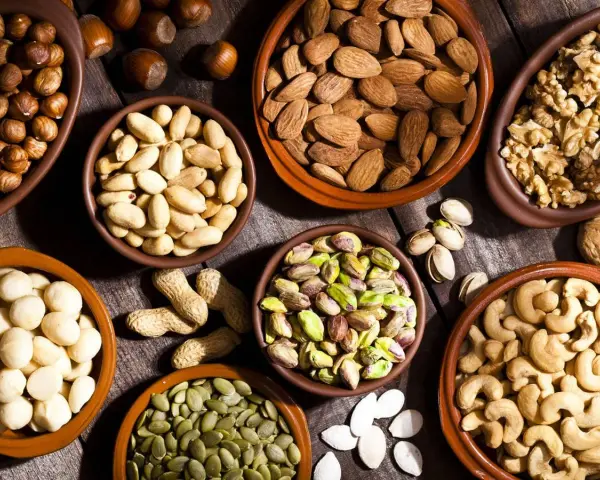Varios cuencos de barro llenos de frutos secos variados: almendras, nueces, pistachos, anacardos, cacahuetes, avellanas y semillas de calabaza.