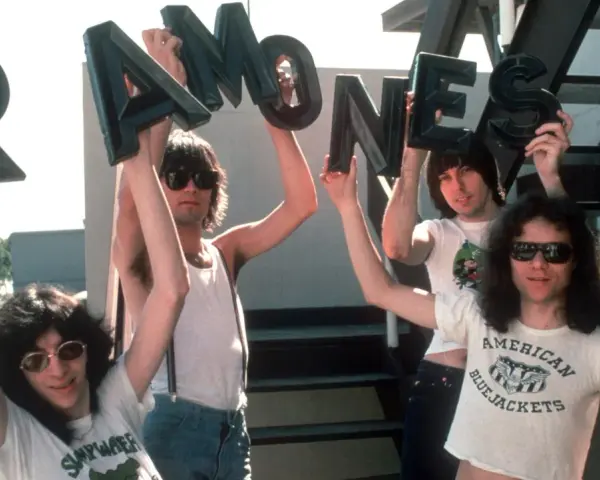 Vier Männer halten die Buchstaben des **titels von Ramones** hoch. Sie tragen Sonnenbrillen und Band-T-Shirts.