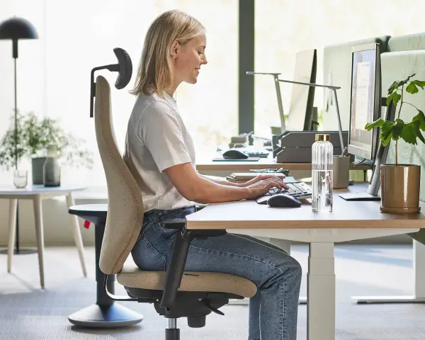 En kvinna sitter ergonomiskt vid ett skrivbord och arbetar vid datorn.