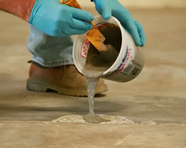 Man con guantes azules vierte hormigón líquido de un cubo para reparar el suelo. Aprende como hacer hormigón para suelo.