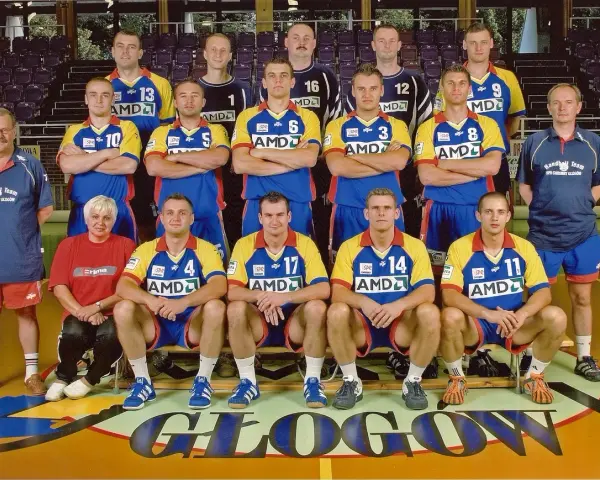 Drużyna SPR Chrobry Głogów pozuje do zdjęcia. Zawodnicy w żółto-niebieskich strojach sportowych, trenerzy i jedna kobieta.