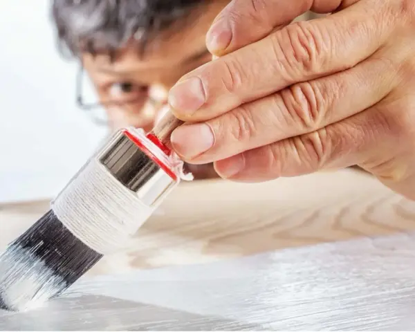 Un uomo applica il primer per legno con un pennello, preparando la superficie per la verniciatura.