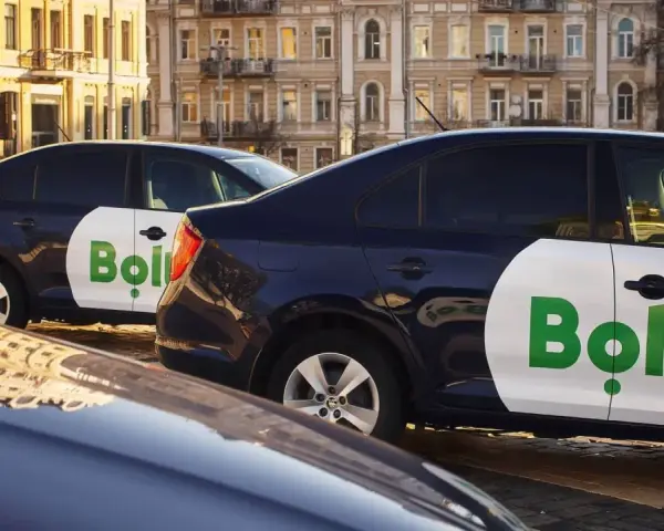 Ciemne samochody z logo Bolt, gotowe do pracy taxi bez licencji, stoją na ulicy.