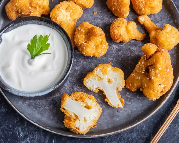 Knusprige Blumenkohl Nuggets aus dem Ofen, goldbraun paniert und mit Sesam bestreut, serviert mit einem cremigen Dip.