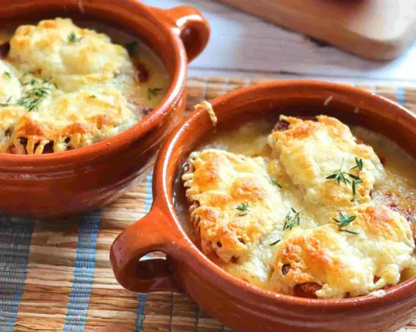 Dos cazuelas de barro con sopa de cebolla gratinada con queso y hierbas.