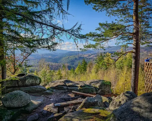 Kamienne skały i ławki na tle rozległej, leśnej panoramy Karkonoszy.