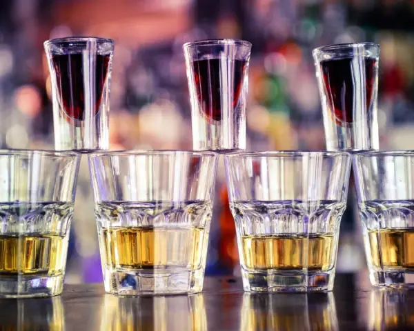 Rzędy kieliszków z bursztynowym alkoholem i ciemnoczerwonym likierem, gotowe do zrobienia jager bomb drink.