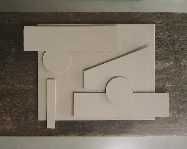 Abstrakt komposition med geometriska former i ljusbeige akrylfärg, arrangerade på en mörk träyta.