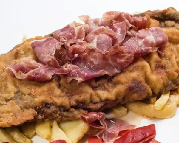 Cachopo asturiano rebozado con jamón serrano encima, acompañado de patatas fritas y pimientos rojos.