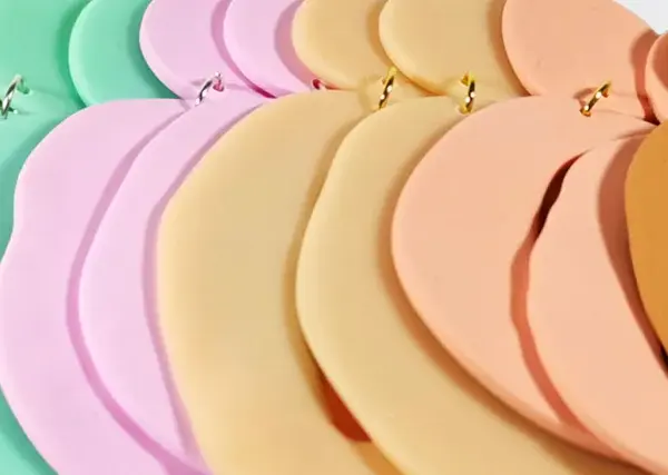 Fimolera smycken i pastellfärger, arrangerade i en mjuk kurva. Grönt, mintgrönt, rosa, beige och orange skapar en drömsk färgpalett.