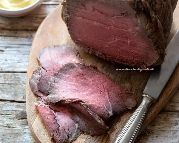 Roast beef ricetta classica: succulento arrosto affettato su tagliere di legno, pronto per essere gustato.