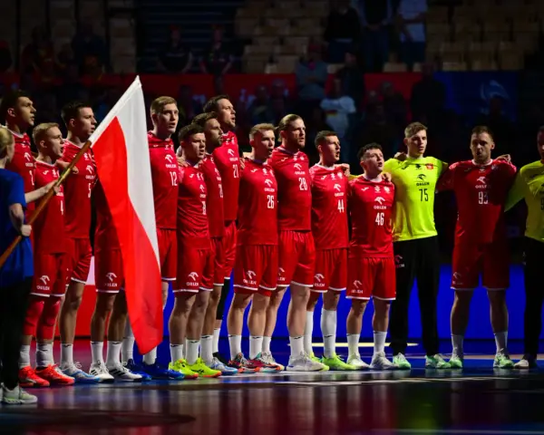Drużyna piłkarzy ręcznych w czerwonych strojach z polską flagą. To ważny moment w 2 lidze piłki ręcznej.