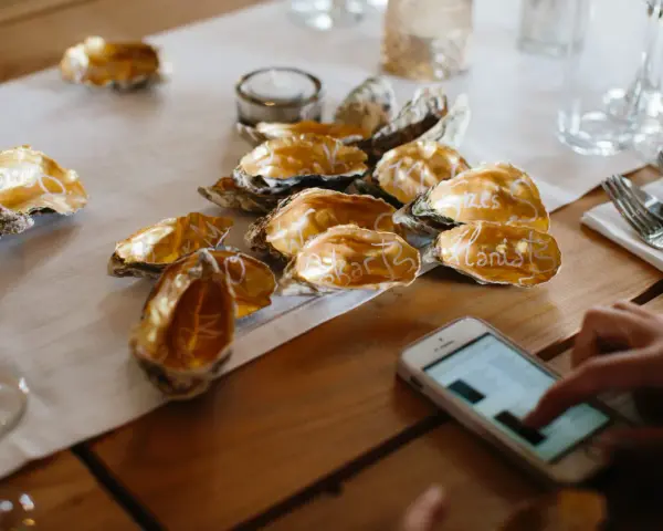 Złote muszle z imionami gości na stole, obok telefon. To symbolika wesela bez telefonów, które zyskują na popularności.