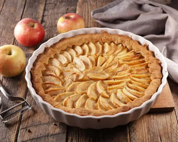Torta di mele umida e soffice, con mele fresche e un pelapatate su un tavolo di legno rustico.