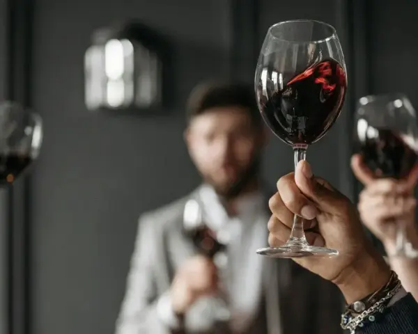 Wzniesione kieliszki z czerwonym winem, w tle mężczyzna w garniturze. Ciesz się chwilą z dobrym winem w kieliszku.