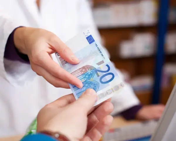 Eine Person in einem weißen Kittel reicht einen 20-Euro-Schein. Möglicherweise zur Bezahlung von Krankengymnastik Kosten.