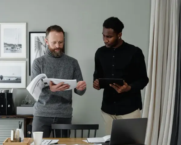 Two men review documents and a tablet, discussing the details of in-kind donation accounting.