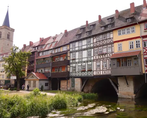 Fachwerkhäuser reihen sich am Wasser entlang, ein Kirchturm ragt empor. Ein idyllischer Anblick, um Erfurt entdecken zu gehen.