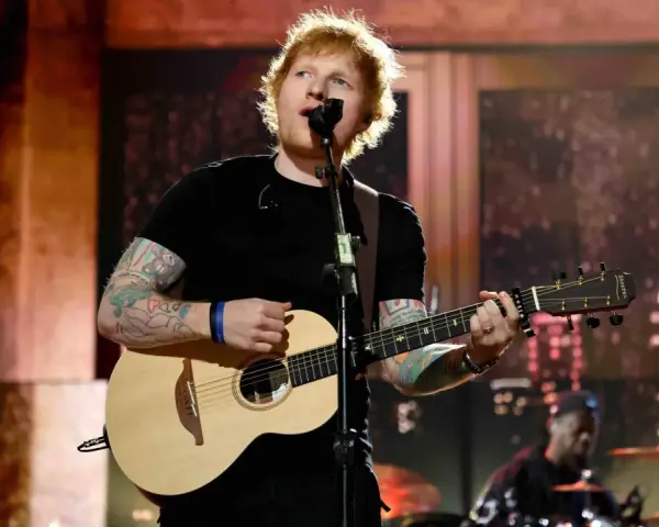 Ed Sheeran spielt Gitarre und singt auf einer Bühne.