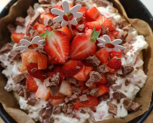 En läcker cheesecake med jordgubbar och chokladbitar, perfekt för ett somrigt cheesecake recept. Blomsterpinnar dekorerar toppen.