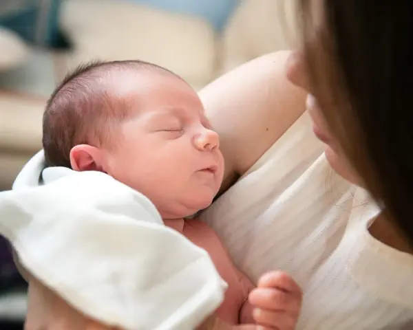 Śpiący noworodek wtulony w ramiona mamy. Delikatne światło podkreśla jego rysy.