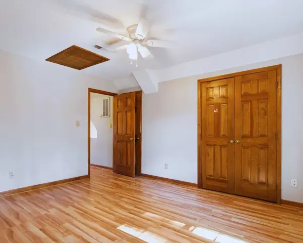 Habitación con suelo de madera clara y puertas de madera oscura, creando un bonito contraste. Un ventilador de techo ilumina el espacio.