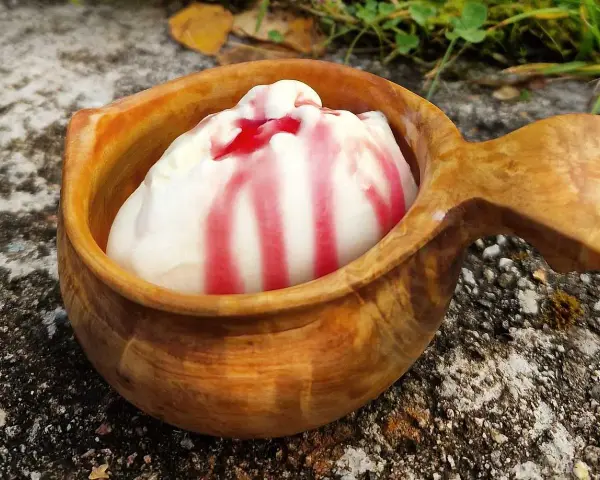 En skopa hemmagjord glass med röd sås i en träkopp, placerad utomhus på sten.