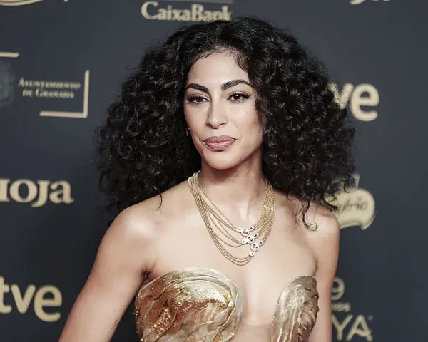 Mujer con espectacular pelo rizado, peinado con volumen y brillo. Luce un vestido dorado y un collar de cadenas.