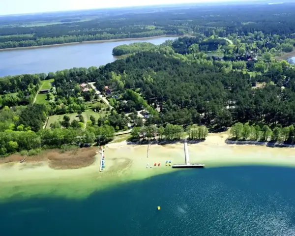 Malownicze warchały jezioro otoczone lasem, z piaszczystą plażą, pomostami i kolorowymi łódkami.