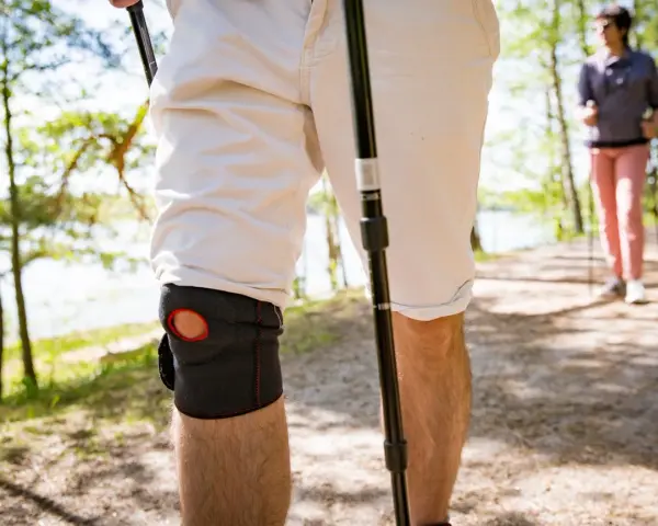 Mann mit Kniebandage beim Nordic Walking. Knieschmerzen beim Bergabgehen beeinträchtigen die Wanderung.