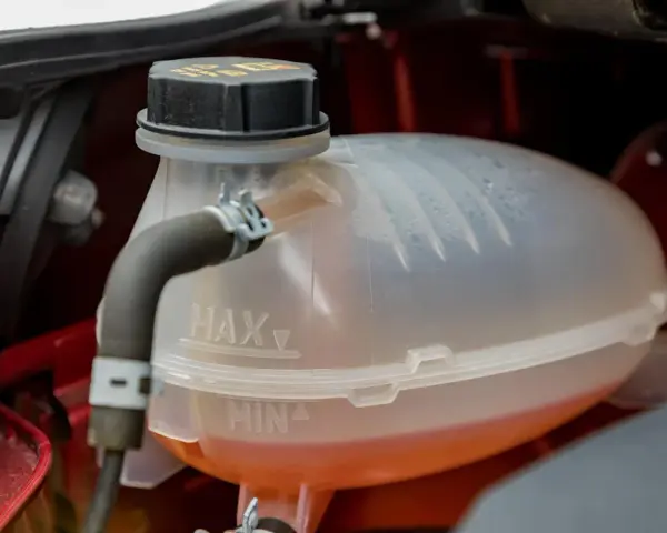 A car's coolant reservoir with MAX and MIN lines. The orange coolant is between the lines, indicating the correct level. This image helps answer "what coolant does my car need.