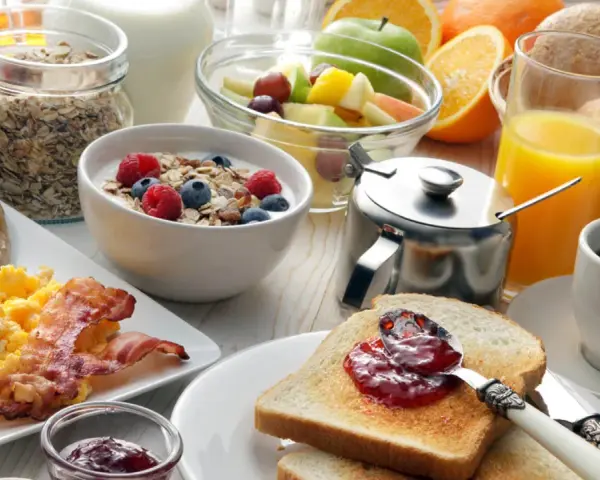 Deftiger Brunch in Schleswig-Holstein: Rührei, Speck, Würstchen, Müsli, Obst, Saft und Kaffee.
