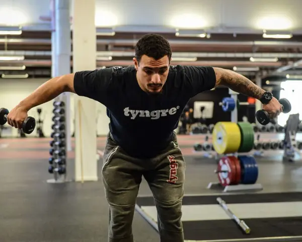 Man tränar baksida axlar med hantlar på gym.