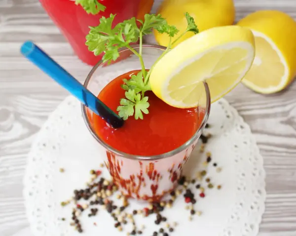 Orzeźwiający drink z sokiem pomidorowym, ozdobiony plasterkiem cytryny i natką pietruszki, gotowy do wypicia.