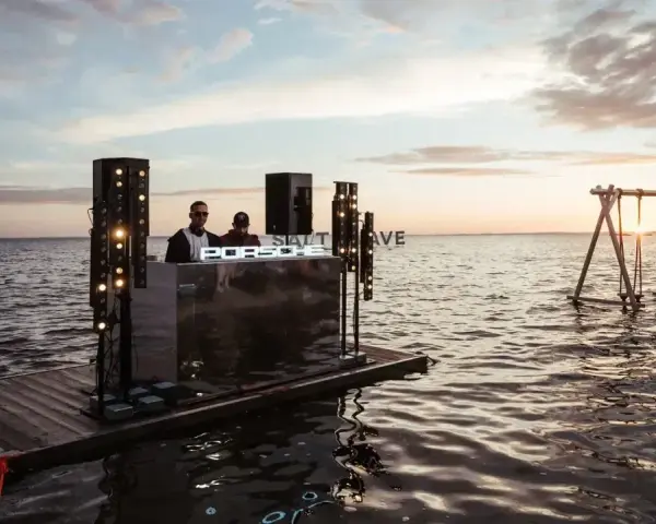 DJ na wodnej platformie podczas Salt Wave Festival. W tle huśtawka na jeziorze o zachodzie słońca.