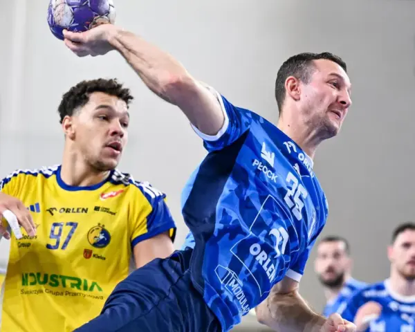Gracz w niebieskiej koszulce rzuca piłkę, podczas gdy przeciwnik w żółtej koszulce z numerem 97 próbuje go zablokować. Emocjonujący mecz piłka ręczna liga mistrzów.