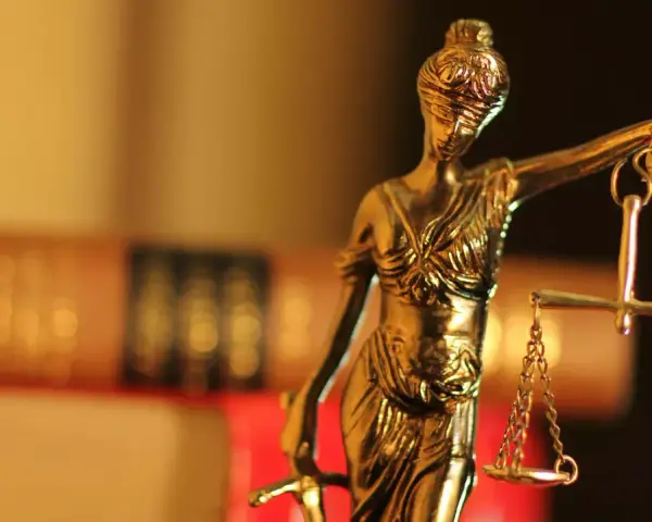 Justitia-Statue mit Waage und Schwert, symbolisiert Gerechtigkeit. Im Hintergrund unscharfe Bücher, die auf einen Fall mit 1/3 Betreuung hindeuten könnten.