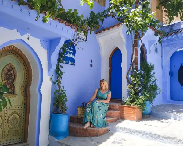 Maj w Maroku to idealna pogoda na zwiedzanie błękitnego miasta Chefchaouen. Kobieta w letniej sukience siedzi na schodach przed Casa Sabila.