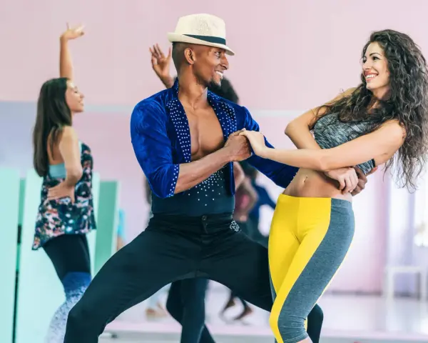 Tancerze w parach ćwiczą bachata co to za taniec. Radosna atmosfera i dynamiczne ruchy.