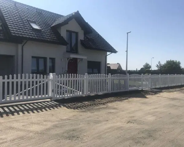 Biały płotek ogrodowy zrób to sam, idealnie otacza dom. Wygląda jak nowy, dodaje uroku posesji.