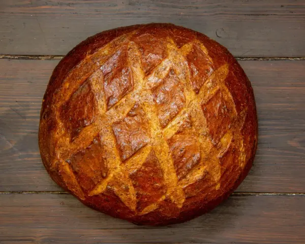 Ein **freigeschobenes Brot** mit knuspriger Kruste und Rautenmuster liegt auf dunklem Holz.
