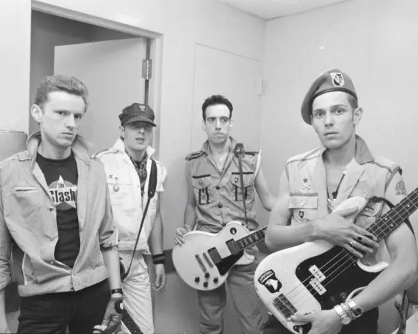 Les membres de The Clash posent avec leurs guitares. L'un porte un t-shirt "The Clash".