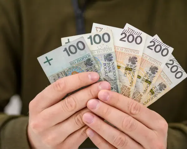 Dłonie trzymają polskie banknoty: 100 i 200 zł. To symbol nagrody za pracę, jak 800 plus tylko dla pracujących.