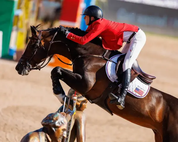 Le cheval Balou du Reventon saute un obstacle, son cavalier en veste rouge le guidant avec précision.