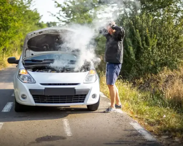 Rozbiegany diesel dymi spod maski. Mężczyzna w rozpaczy łapie się za głowę, stojąc przy białym samochodzie na poboczu drogi.