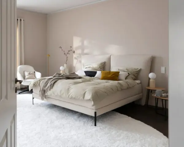 Beige Schlafzimmer Ideen: Einladendes Bett mit beiger Bettwäsche, Akzentkissen und Decke. Weißer Sessel und Teppich schaffen Gemütlichkeit.