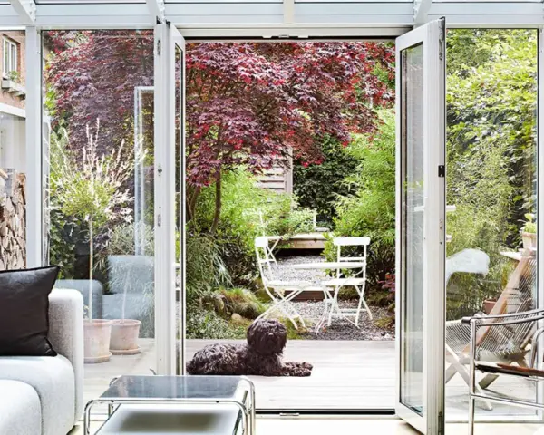 Gemütliches Wohnzimmer mit Blick in den Garten. Ein Hund liegt auf der Holzterrasse, ideal zum Wintergarten einrichten.