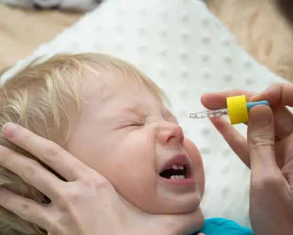 Ein Baby weint, während ihm N सेंटropfen verabreicht werden.