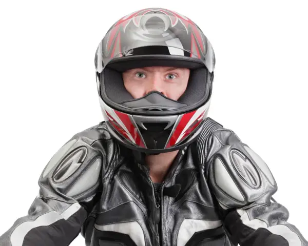 Occhi spalancati dietro un casco stretto, pronto per la corsa. La tuta in pelle grigia e nera completa il look da motociclista.