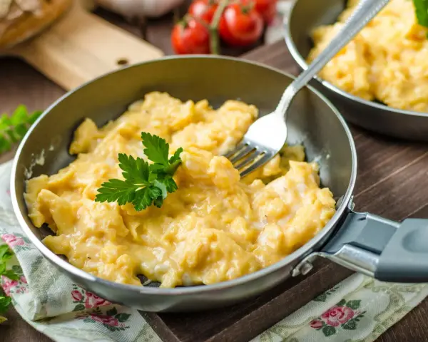 Pyszna jajecznica z dodatkami, podana na patelni, udekorowana natką pietruszki. Idealna na śniadanie.